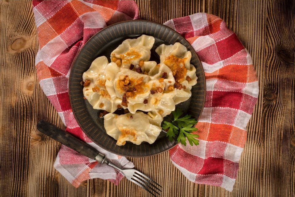 Ein dunkler Teller Pierogi mit gebratenen Beilagen und Petersilie, angerichtet auf einem karierten Tuch auf einem Holztisch.