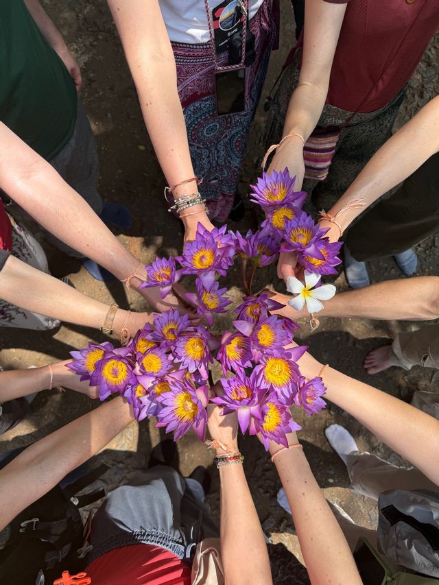 Un gruppo WeRoad si stringe in cerchio, tenendo insieme un grande bouquet di fiori di loto viola e gialli.