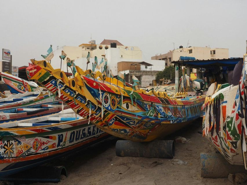 Barcos tradicionales bellamente pintados con patrones coloridos, banderas y un ojo grande, descansando en una playa de arena.