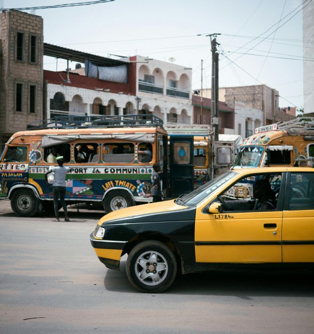 Un taxi amarillo y negro en una carretera pavimentada con un autobús colorido y otros vehículos al fondo.