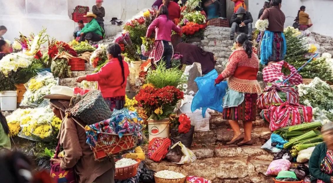 Un affollato mercato di fiori all'aperto su una scalinata di pietra, con persone in abiti tradizionali che acquistano e vendono bouquet colorati.