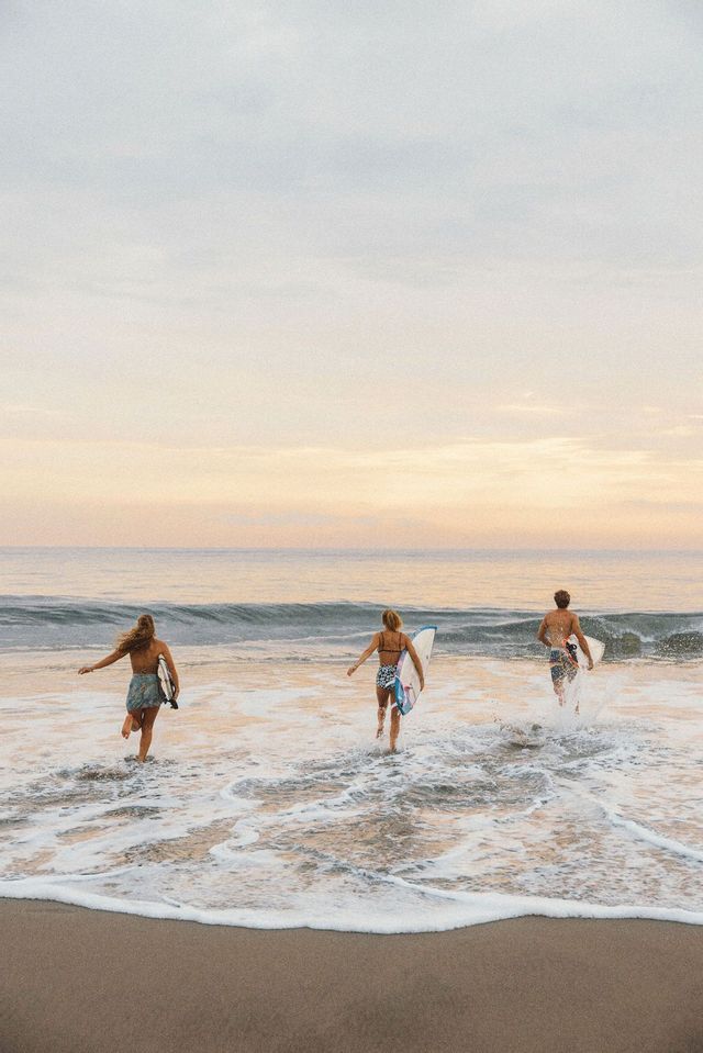 Un viaggio di gruppo WeRoad con tre surfisti che corrono nell'oceano con le loro tavole da surf all'alba.