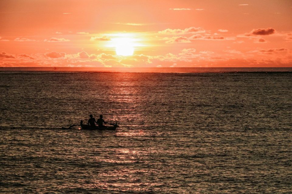 Silhouette di due persone in barca sull'oceano durante un vibrante tramonto arancione.