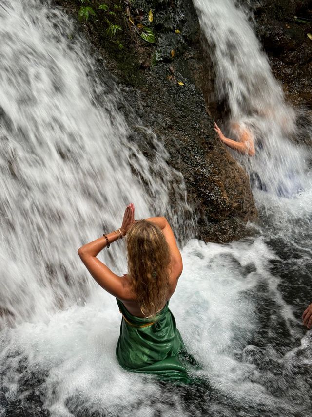 Una donna di un viaggio di gruppo WeRoad, ripresa di spalle, in posa di preghiera nell'acqua impetuosa di una cascata.