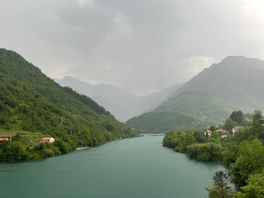 Une rivière turquoise serpente à travers une vallée entre des montagnes verdoyantes et luxuriantes sous un ciel nuageux.