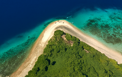 Vue aérienne d'un voyage de groupe WeRoad sur la pointe d'une flèche sablonneuse couverte d'arbres verts, entre des eaux bleu profond et turquoise.