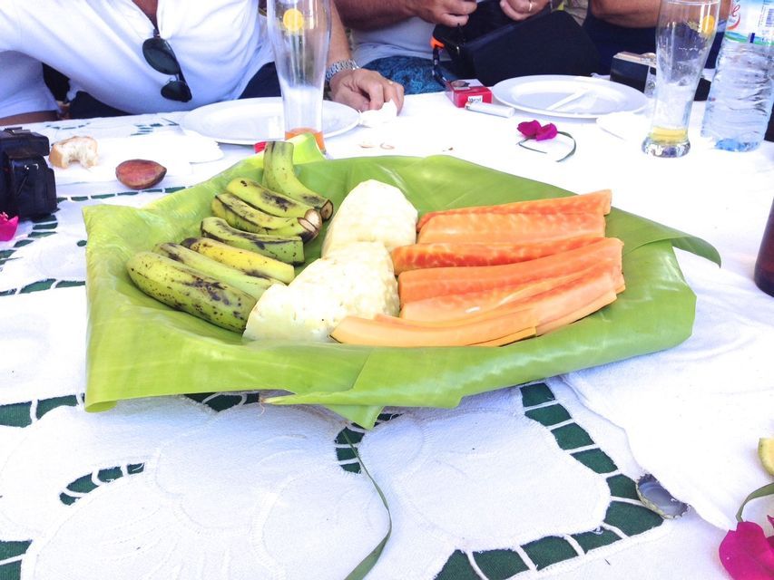Sur une nappe blanche, un plateau confectionné à partir d'une grande feuille verte présente des tranches de papaye, d'ananas et de bananes vertes.