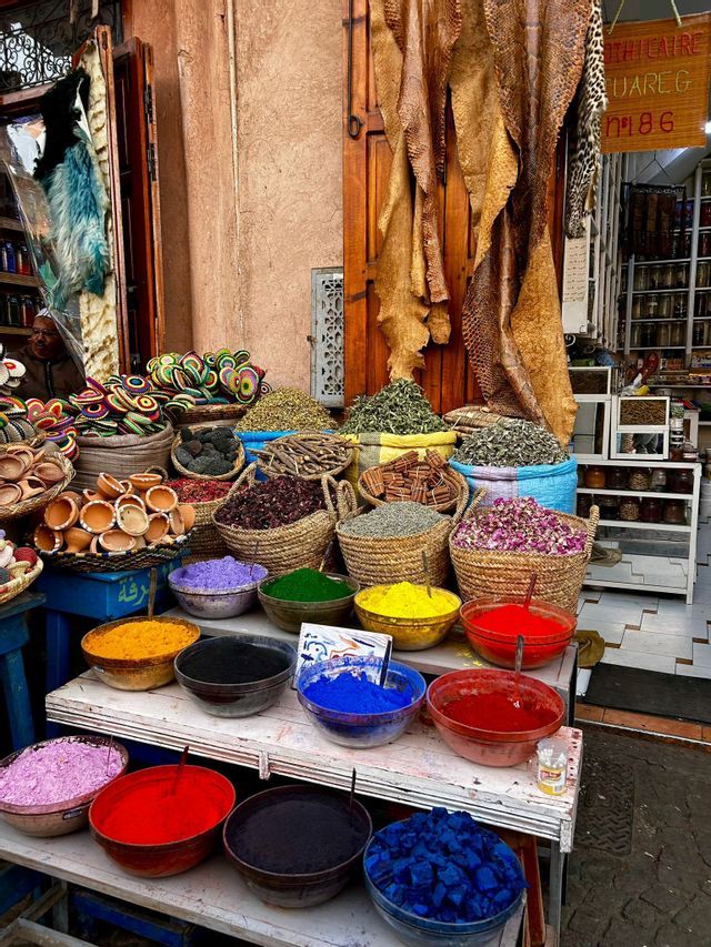 Un puesto de mercado exhibe coloridos pigmentos en polvo en cuencos y cestas tejidas llenas de hierbas y especias.