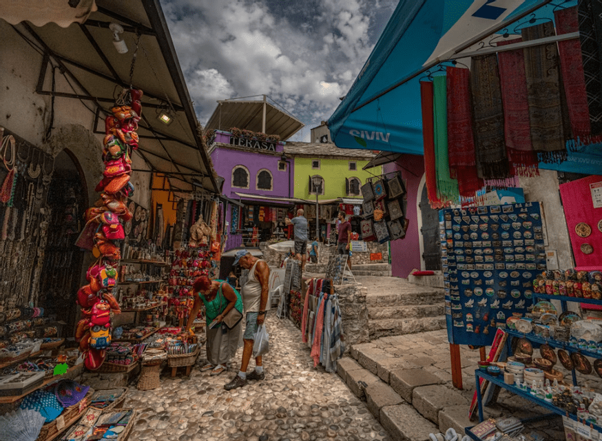 Les gens flânent devant les étals de souvenirs et de textiles d'un marché en plein air, dans une rue pavée étroite, entre des bâtiments colorés.