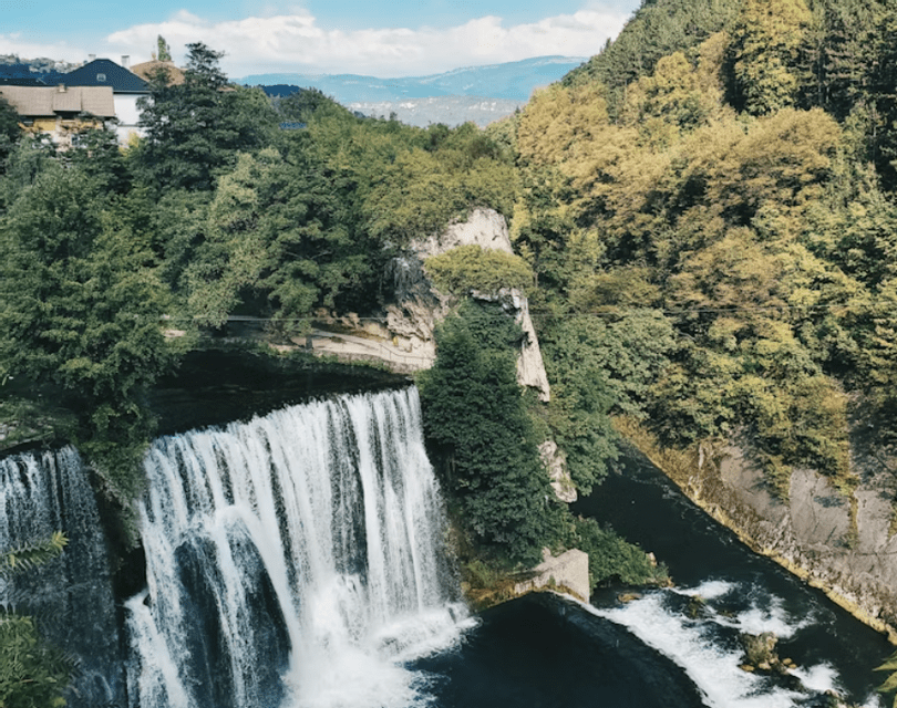 Une grande cascade se jette dans une rivière, entourée d'une forêt verdoyante, avec des maisons à flanc de colline en arrière-plan.
