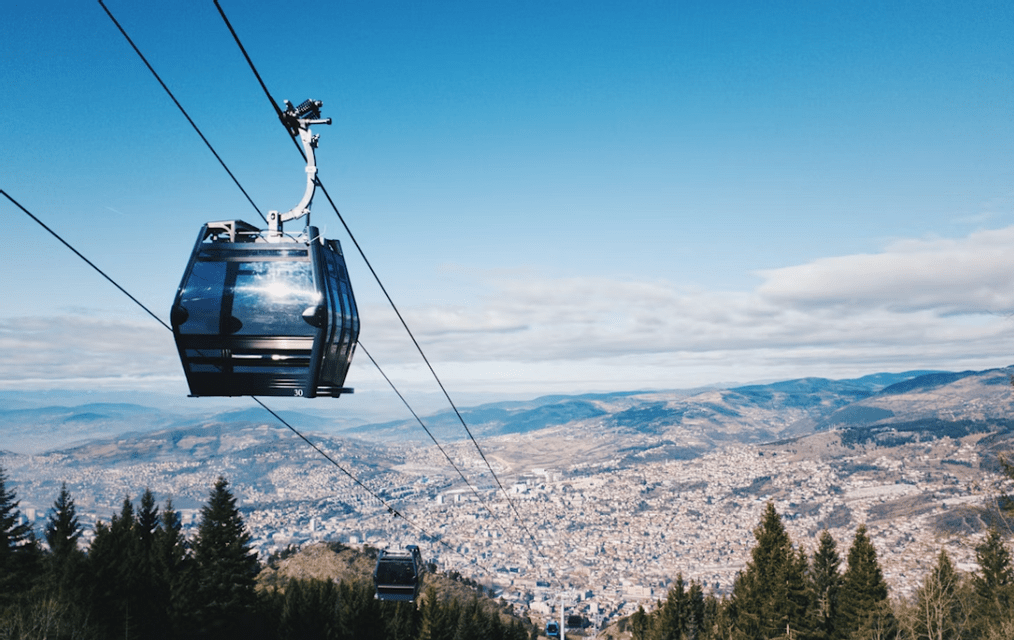 Un téléphérique moderne survole une ville tentaculaire dans une vallée montagneuse, avec des cimes d'arbres persistants en contrebas.