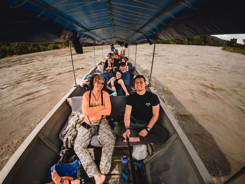 Eine WeRoad Gruppenreise fährt in einem Longtail-Boot auf einem breiten Fluss, mit zwei Männern, die im Vordergrund für ein Selfie lächeln.