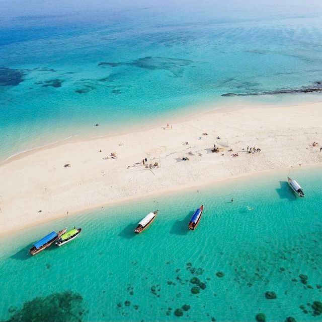 Vue aérienne d'un banc de sable blanc entouré d'eaux turquoise, avec plusieurs bateaux à longue queue amarrés.