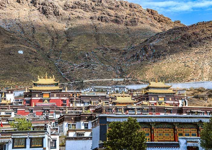 Un gruppo di edifici monastici in stile tibetano con tetti dorati, adagiati alla base di una montagna rocciosa.