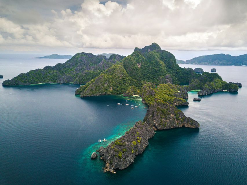 Una vista aerea di isole verdi e lussureggianti e affioramenti rocciosi in un oceano turchese e blu profondo sotto un cielo nuvoloso.