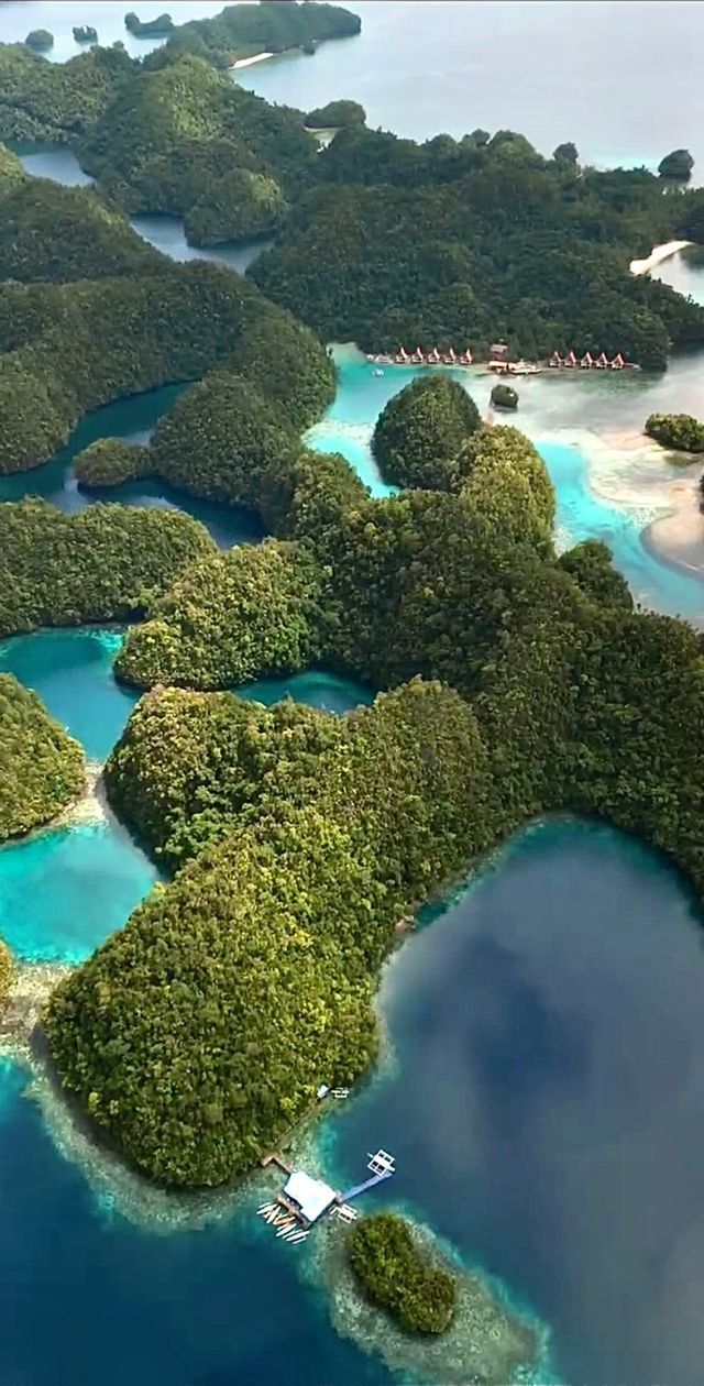 Una vista aerea di numerose piccole isole verdi sparse in acque calme, turchesi e blu profondo.