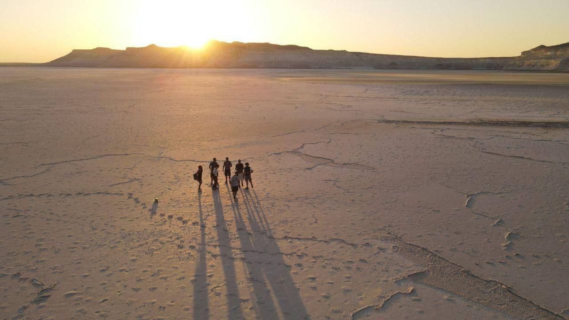 Vista aerea di un gruppo WeRoad in viaggio nel vasto deserto al tramonto, con lunghe ombre.