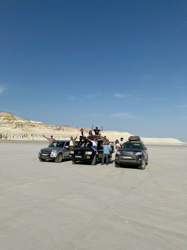Un gruppo WeRoad in posa per una foto con tre SUV in un vasto paesaggio arido e scogliere bianche sullo sfondo.