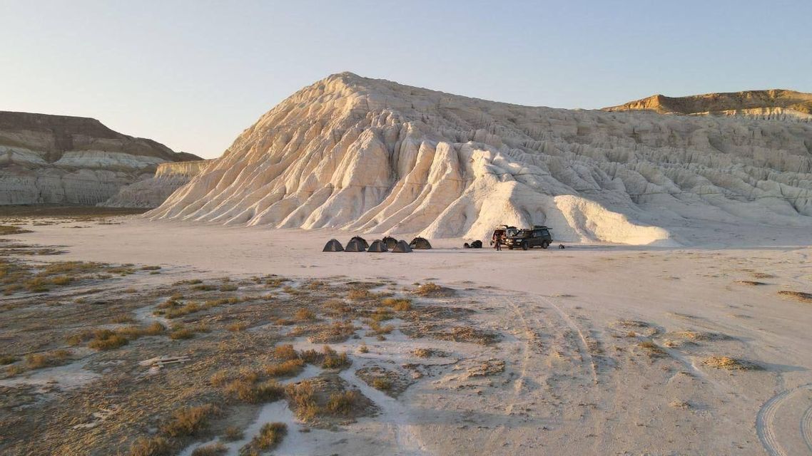 Un campeggio per un viaggio di gruppo WeRoad con tende e un SUV ai piedi di una vasta montagna bianca in un paesaggio arido.