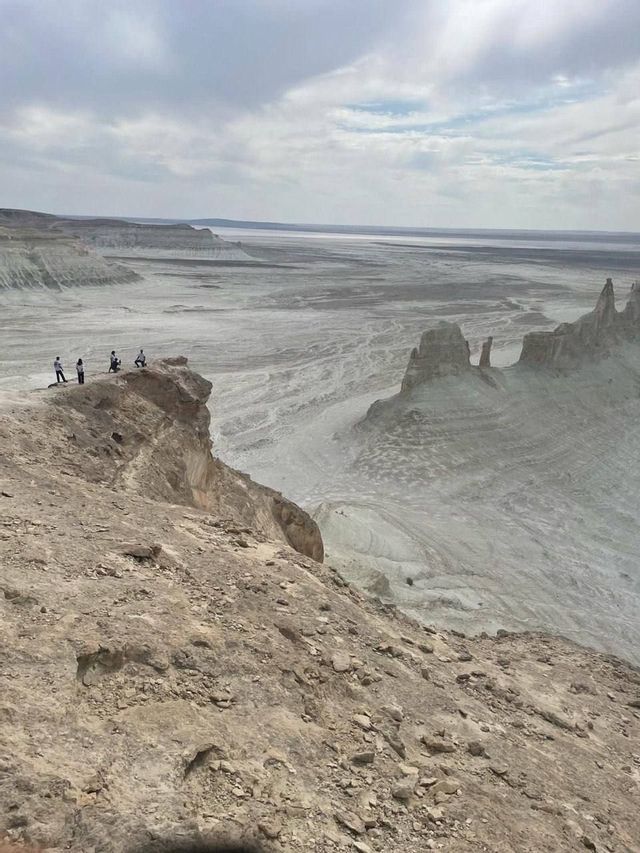 Un gruppo WeRoad di quattro persone in piedi sul bordo di una scogliera rocciosa, affacciato su un vasto canyon arido con guglie di roccia sotto un cielo nuvoloso.