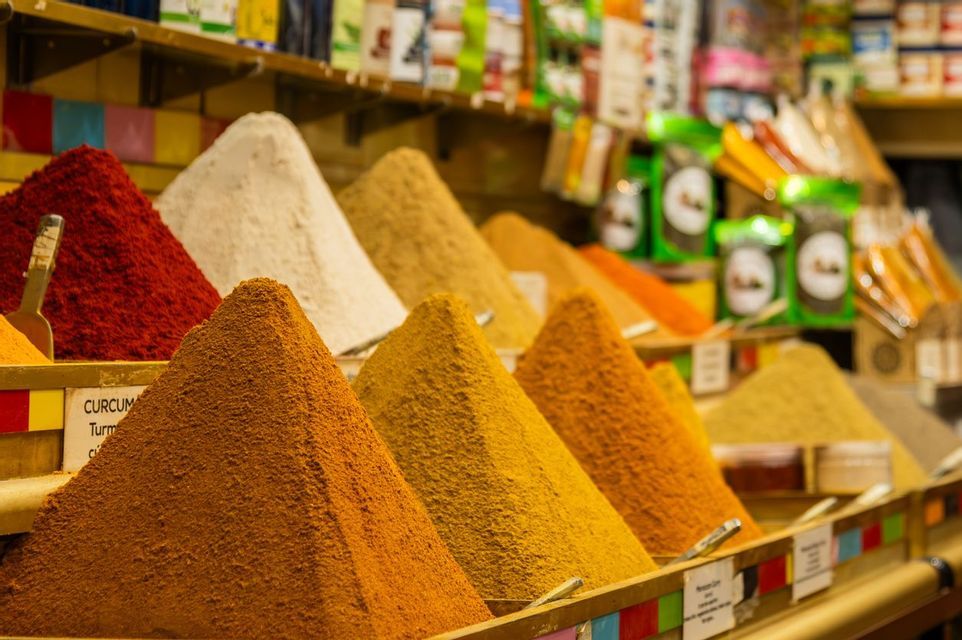 Colorful piles of ground spices arranged in cones in wooden bins at a market stall.