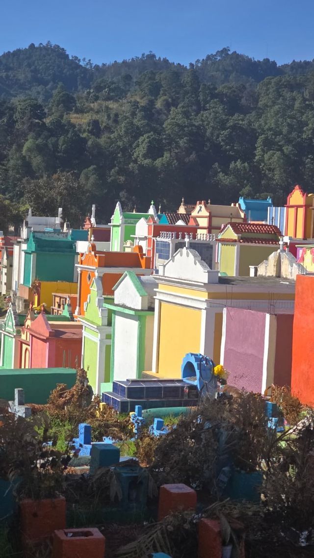 Tumbas y mausoleos coloridos y vívidamente pintados en un cementerio al pie de una colina boscosa bajo un cielo azul claro.