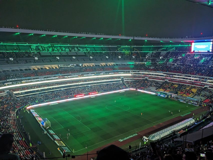 A high-angle view of a football stadium at night, filled with spectators, with the pitch and stands illuminated by green lights.