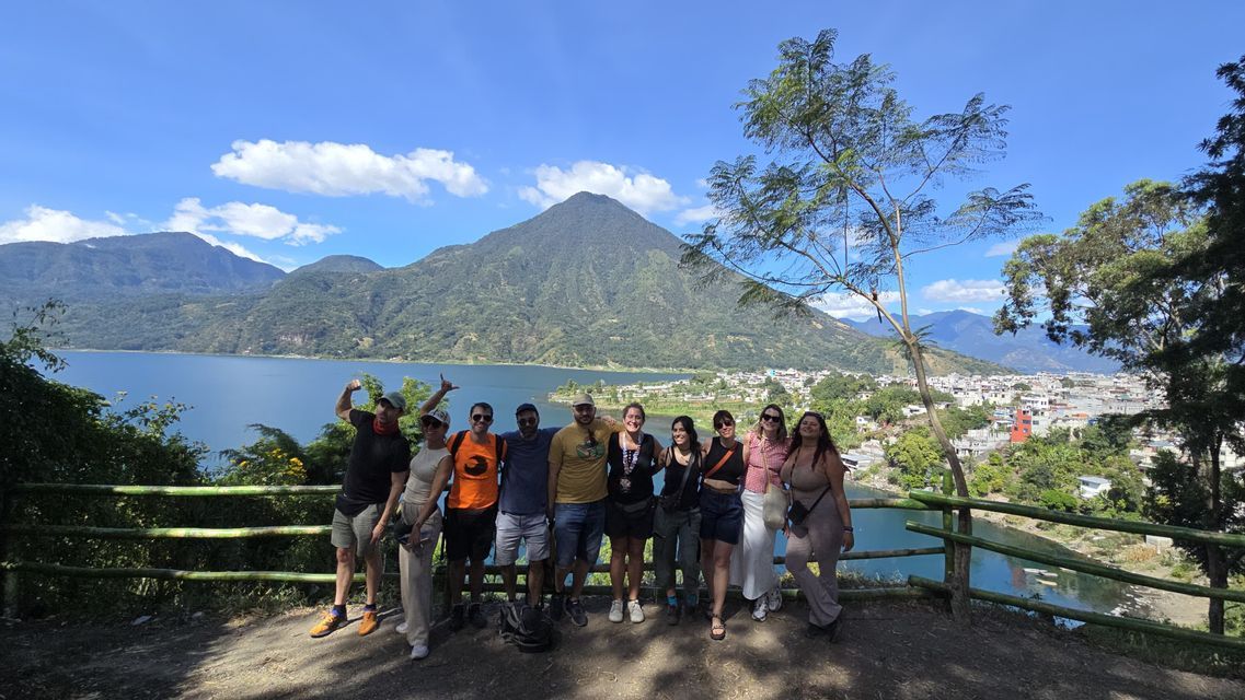 Un viaje en grupo de WeRoad sonríe para una foto en un mirador panorámico con un gran lago, montañas y un pueblo de fondo.