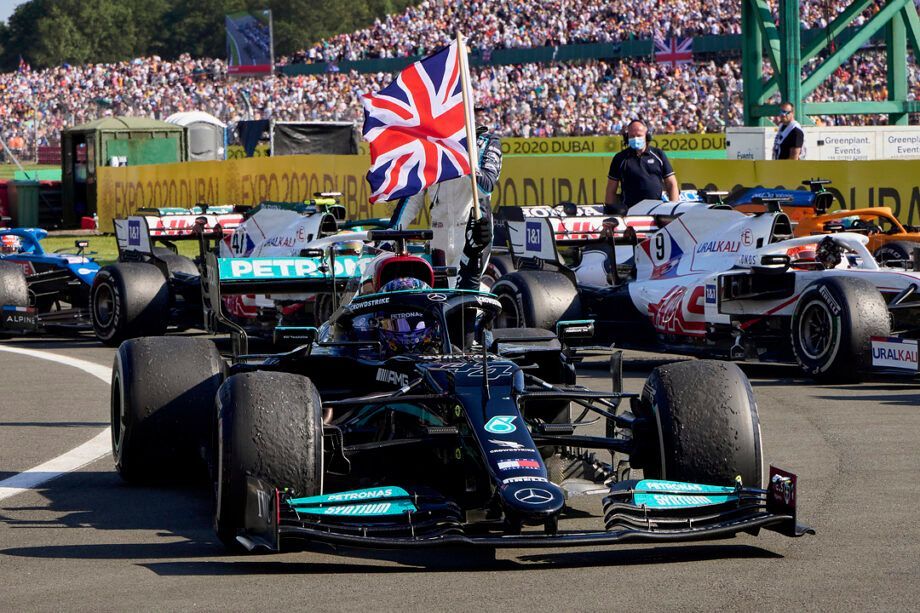 A black Formula 1 car on a racetrack with a person holding a British flag and a crowd of spectators in the background.