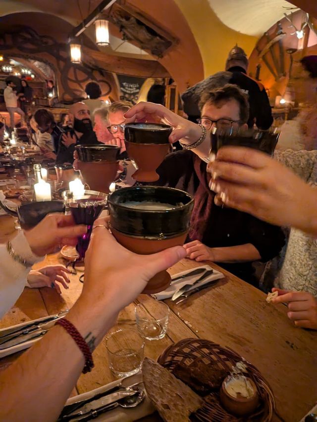 Un viaggio di gruppo WeRoad che brinda con calici in ceramica a un lungo tavolo di legno in un ristorante rustico e con luce soffusa.