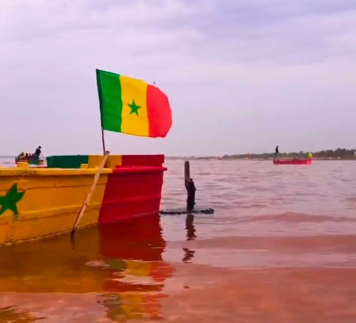 Un barco colorido con la bandera de Senegal flota en aguas de color rosa rojizo bajo un cielo nublado.
