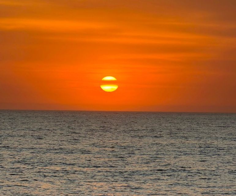 La puesta de sol sobre el océano, proyectando un profundo resplandor naranja en el cielo sobre el agua.