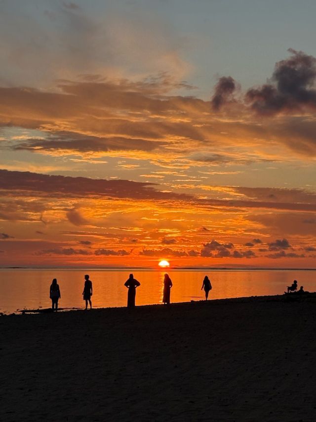 Silhouettes d'un groupe WeRoad sur une plage, observant le soleil orange se coucher sur l'océan calme.