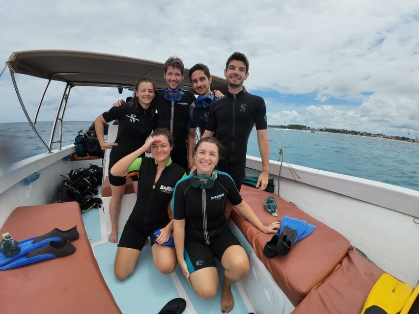 Un voyage de groupe WeRoad en combinaisons de plongée posant pour une photo sur un bateau avant une plongée en pleine mer.
