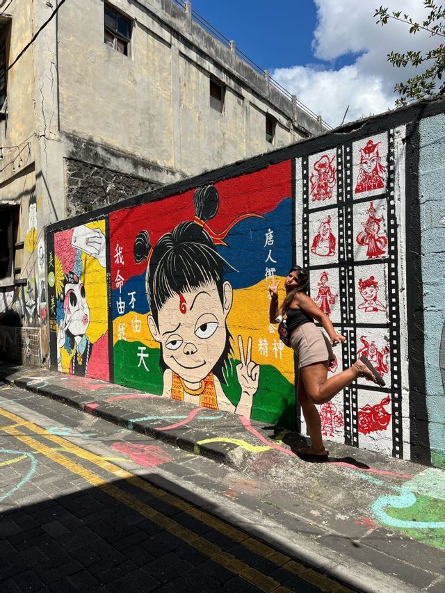 Une femme souriante fait le signe de la paix devant une fresque murale d'art de rue colorée, ornée d'un grand personnage de dessin animé.