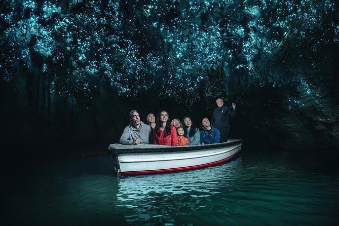 A WeRoad group trip sits in a small boat inside a dark cave, looking up at a ceiling covered in bright blue glowworms.