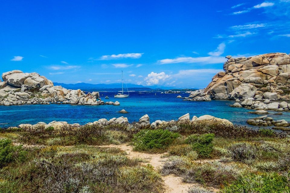 Ein weißes Segelboot ankert in einer ruhigen, türkisfarbenen Bucht, eingerahmt von großen, glatten Felsformationen unter strahlend blauem Himmel.