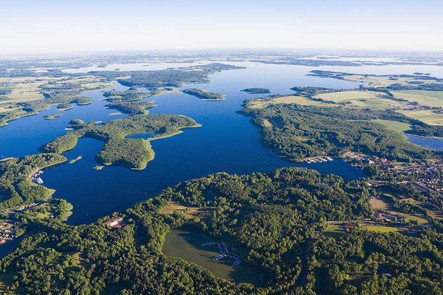Vue aérienne d'une vaste région des lacs, avec des îles verdoyantes et boisées parsemant l'eau d'un bleu profond sous un ciel dégagé.