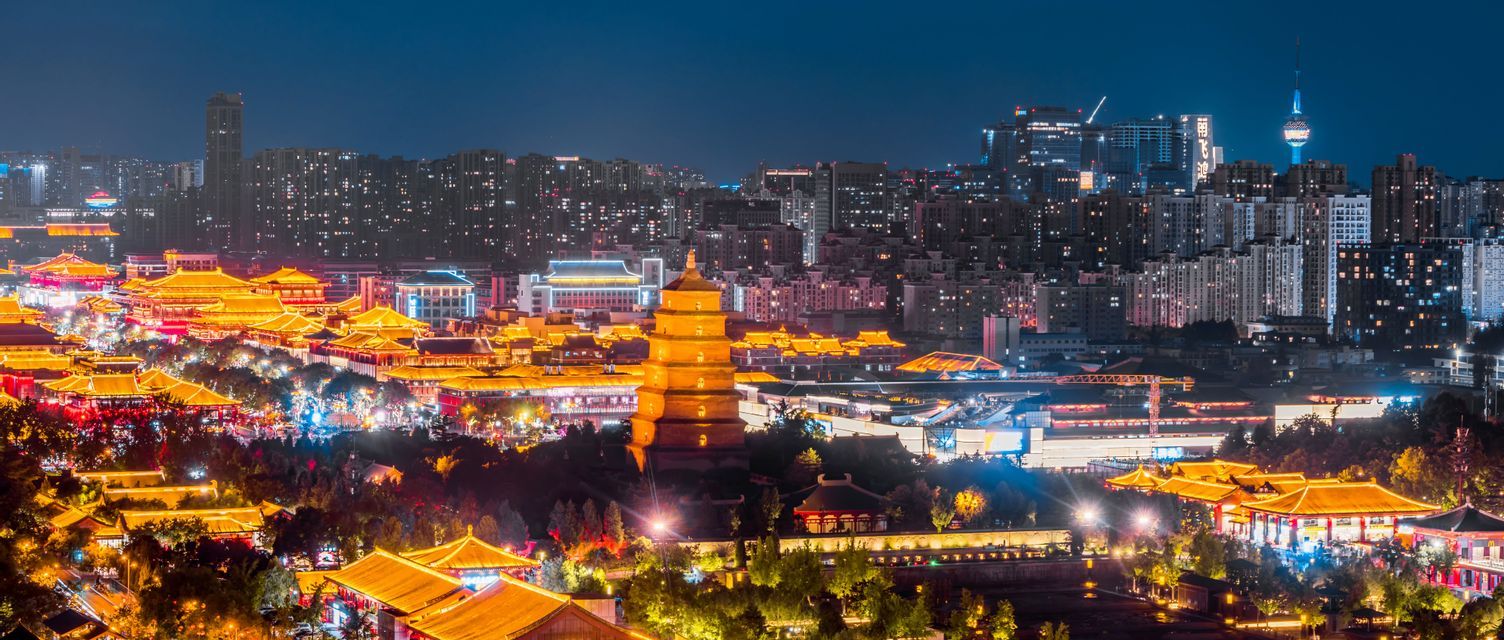 Vista notturna panoramica di un'antica pagoda splendidamente illuminata e di edifici tradizionali contro lo skyline di una città moderna.