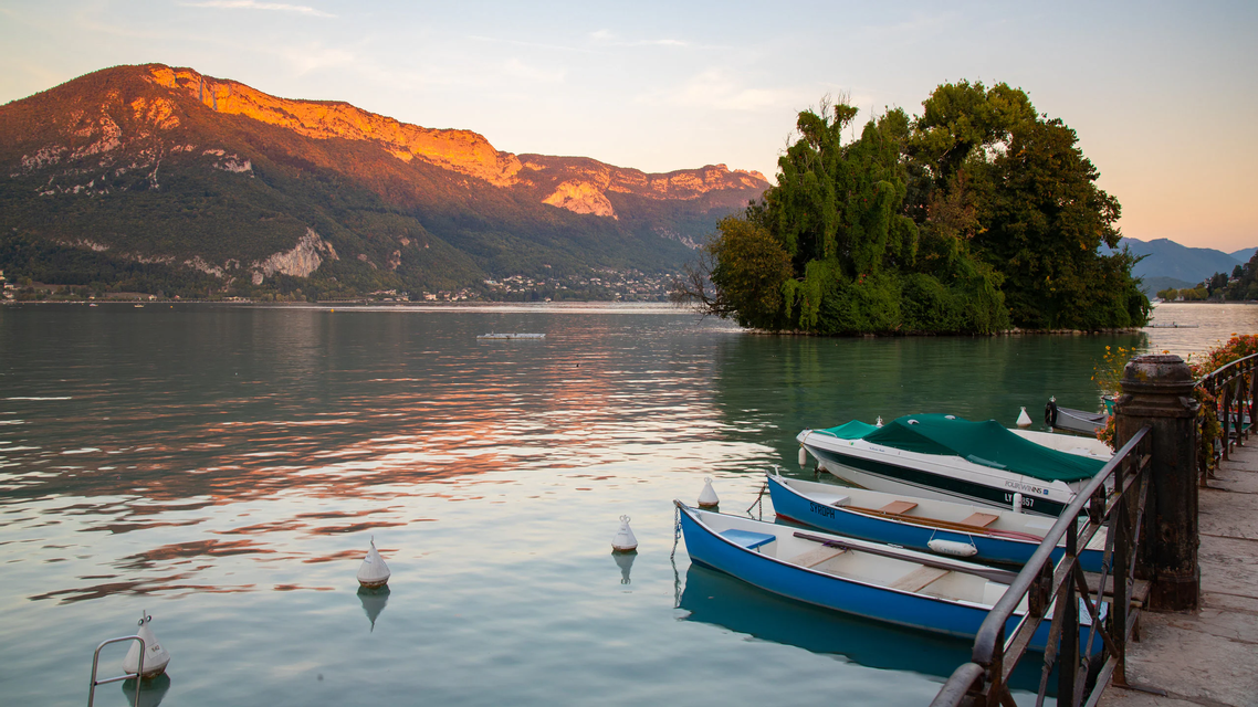 Small boats moored on a calm lake with mountains in the background illuminated by the golden light of sunset.