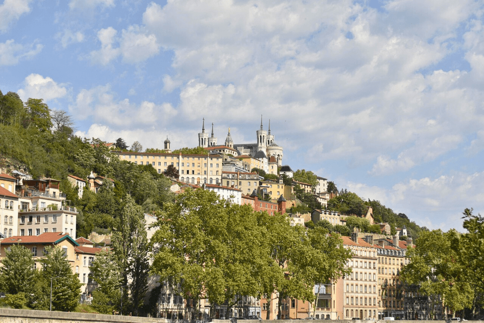 Une ville avec une basilique à son sommet est bâtie à flanc de colline verdoyante sous un ciel partiellement nuageux.