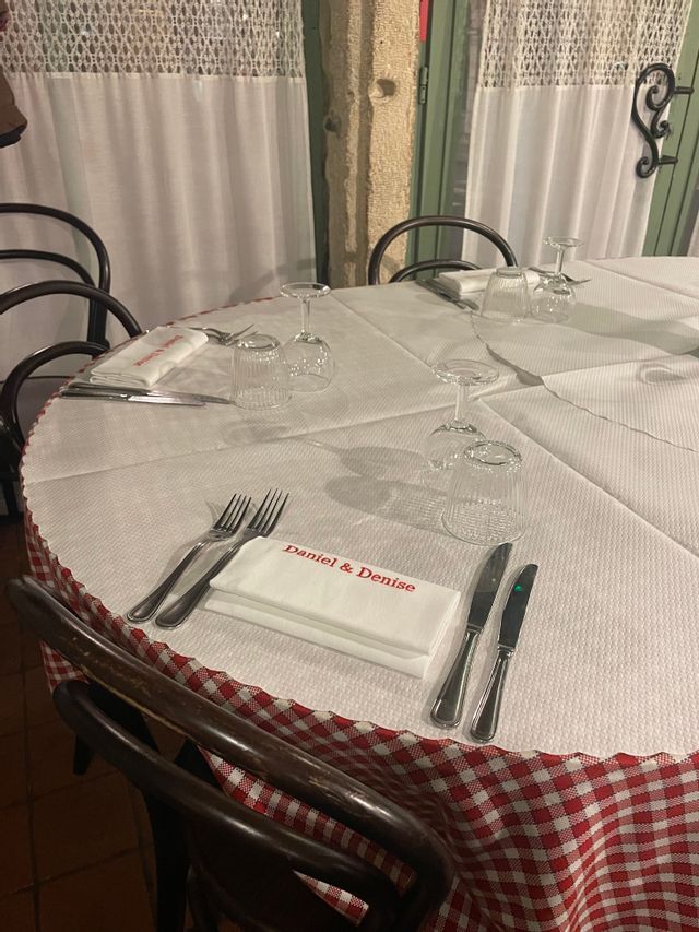 Une table dressée dans un restaurant avec une nappe à carreaux rouges et blancs, des couverts, des verres et une serviette imprimée 'Daniel & Denise'.