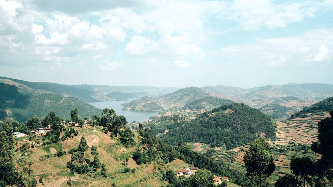 Ein weiter Blick auf terrassierte grüne Hügel, kleine Dörfer und einen sich schlängelnden See unter einem teils bewölkten Himmel.