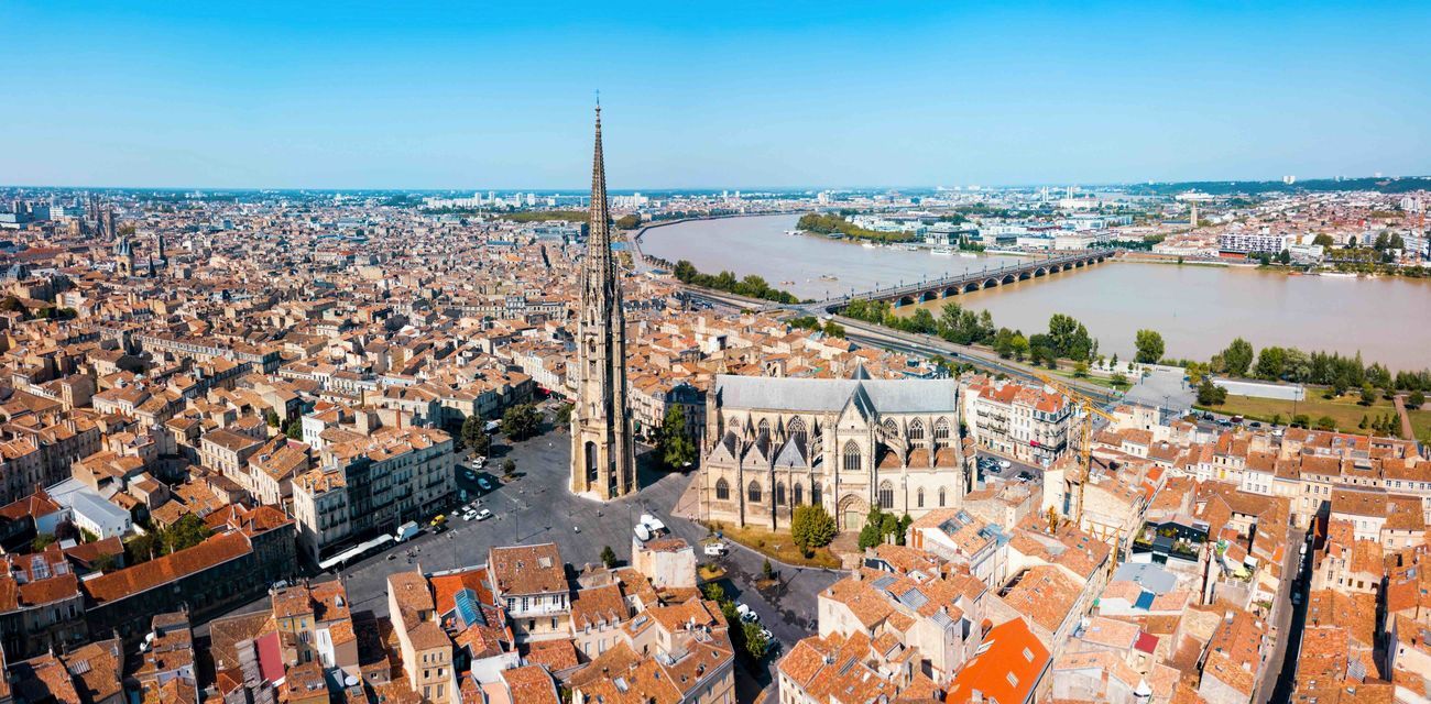 Vue aérienne d'une ville européenne historique avec une grande cathédrale gothique, des toits en terre cuite et un large fleuve en arrière-plan.