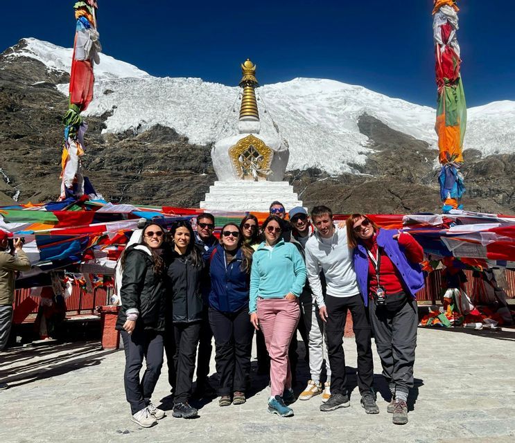 Un viaggio di gruppo WeRoad posa per una foto davanti a uno stupa bianco e bandiere di preghiera, con una montagna innevata sullo sfondo.