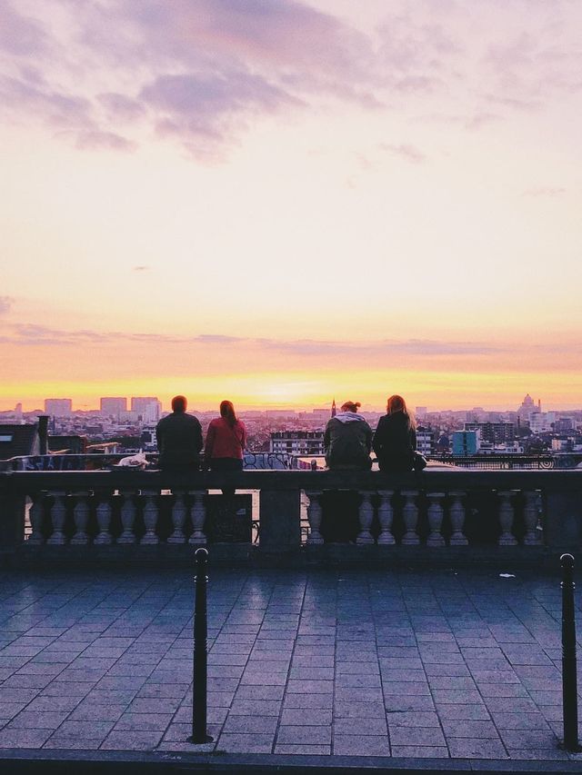 Eine WeRoad-Gruppenreise von vier Personen, die mit dem Rücken zur Kamera auf einer Steinbalustrade sitzen und bei Sonnenuntergang auf eine Stadtkulisse blicken.