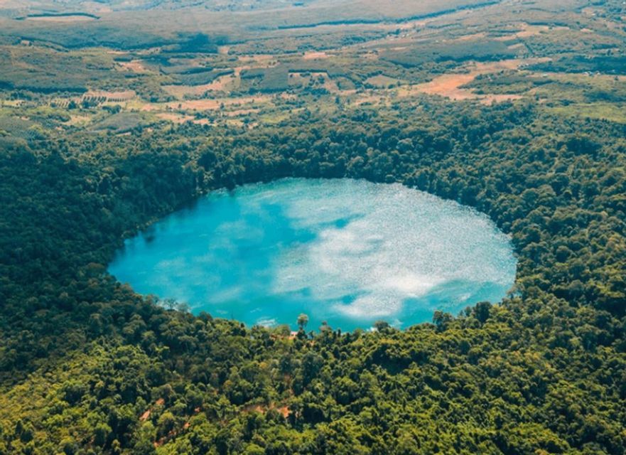 Veduta aerea di un lago craterico circolare turchese, circondato da una fitta foresta verde.