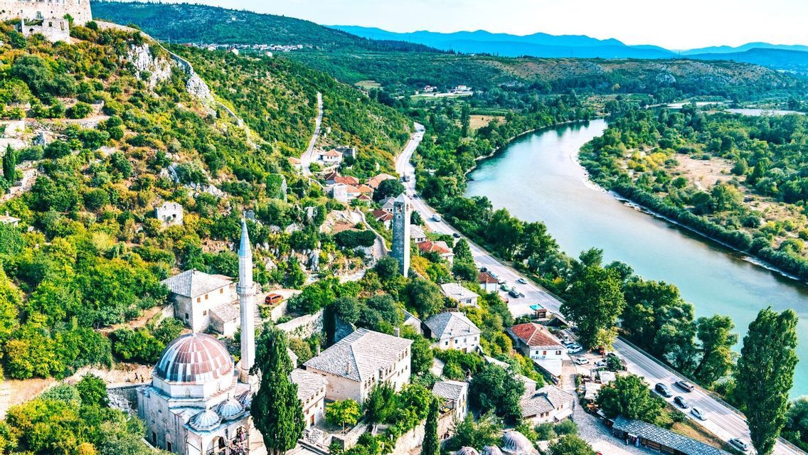 Eine Luftaufnahme einer historischen Stadt mit einer Moschee und einem Uhrturm, gebaut auf einem grünen Hügel neben einem gewundenen Fluss.