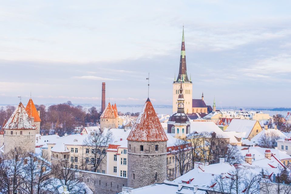 Eine Stadtsilhouette einer historischen Stadt im Winter, mit schneebedeckten Dächern, Steintürmen mit roten Dächern und einem hohen Kirchturm.