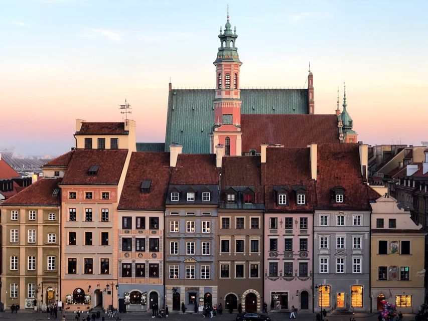 Edificios coloridos y tradicionales y la torre de una catedral en una plaza histórica al atardecer.